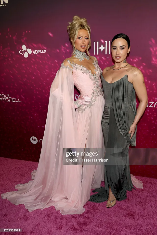 Demi Lovato posing beside another person in a grey gown and heels.