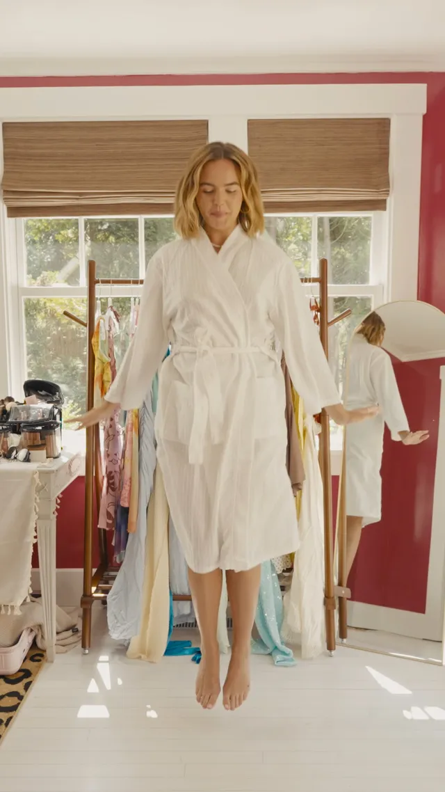Bailee Madison standing barefoot in a white robe indoors.
