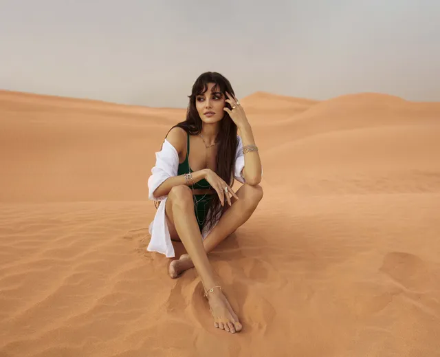 Hande Erçel sitting barefoot in the desert in a white blazer.