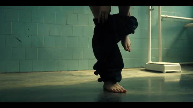 Grace Van Patten stepping barefoot beside dark trousers in a film scene.