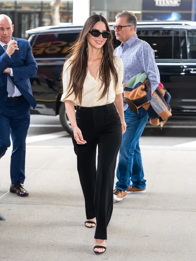 Olivia Munn walking outdoors in trousers and black heels.