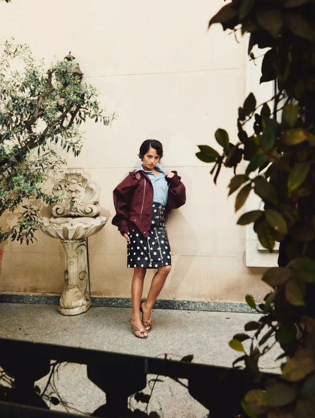 Isabela Merced wearing a patterned dress, burgundy jacket and heeled sandals.