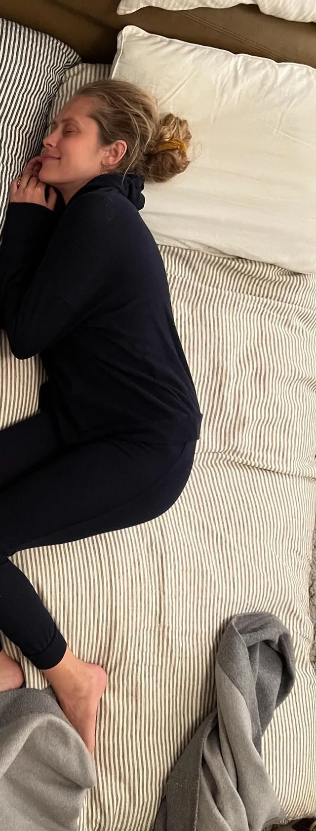 Teresa Palmer resting on a bed in a dark casual outfit.