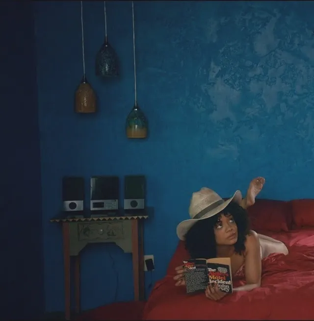 Tessa Thompson reading while reclining on a red sofa.