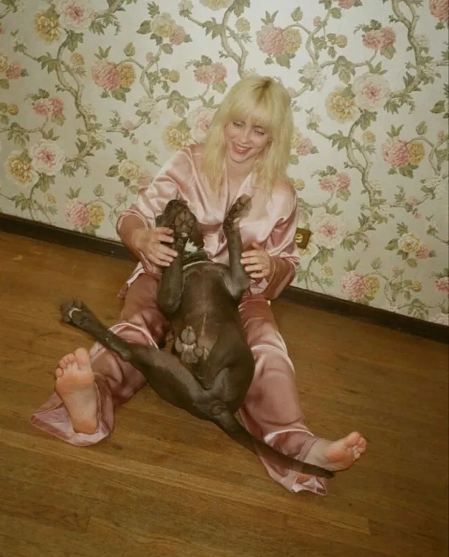 Billie Eilish a seated pink outfit beside a dog.