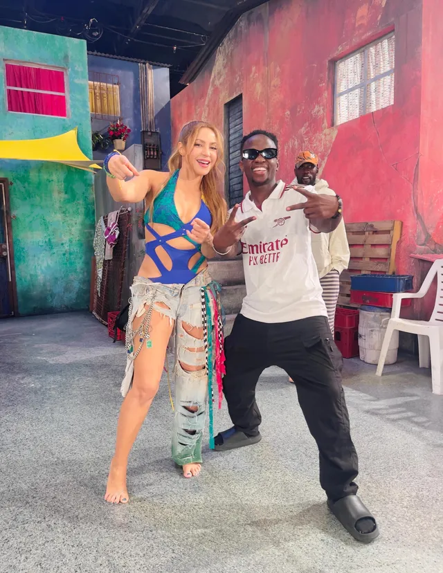 Shakira standing barefoot beside a man in a colorful outfit.