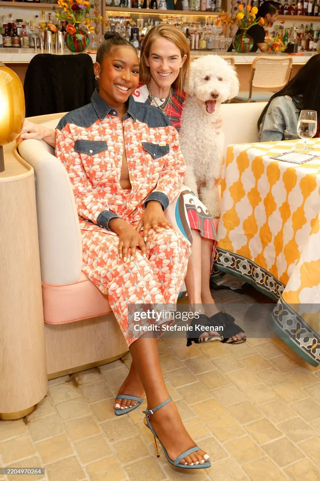 Carlacia Grant sitting beside a guest and a dog in a patterned suit and heels.