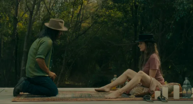 Rebecca Ferguson sitting barefoot on a wooden platform among trees in a film scene.