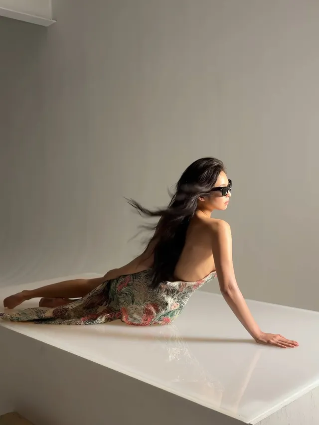 Jennie Kim reclining barefoot on a pale surface in a patterned skirt.