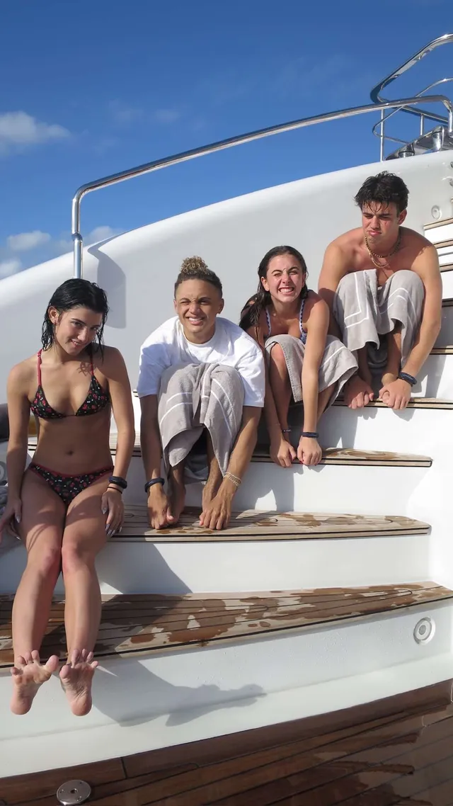 Charli D’Amelio sitting barefoot with friends on boat steps.