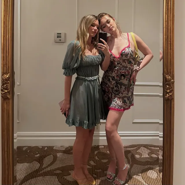 Lola Tung taking a mirror selfie with a friend in a patterned dress and heels.