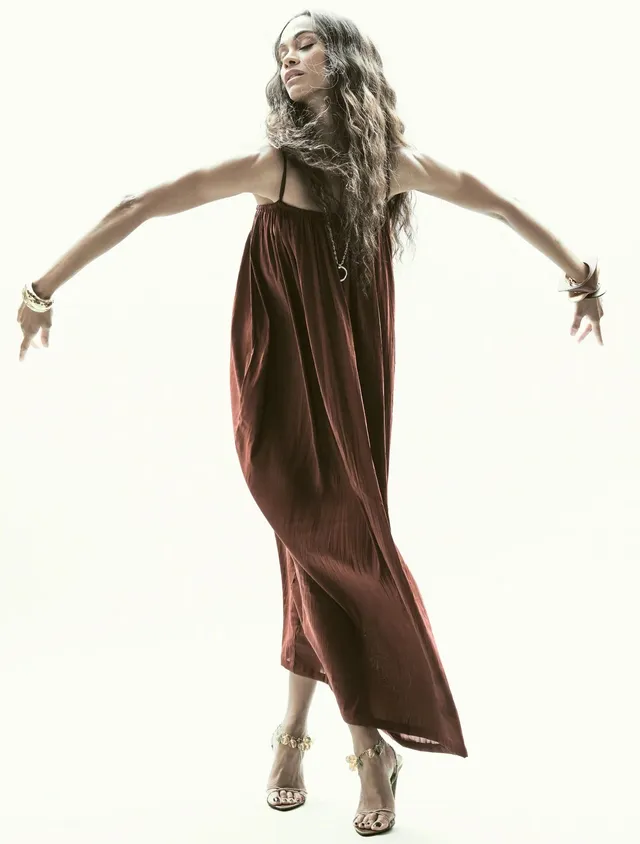 Zoe Saldaña posing in a flowing brown dress.