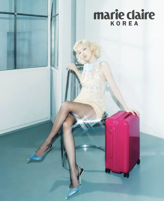Rosé sitting on a pink suitcase in a pale dress and pointed-toe high heels for an editorial.