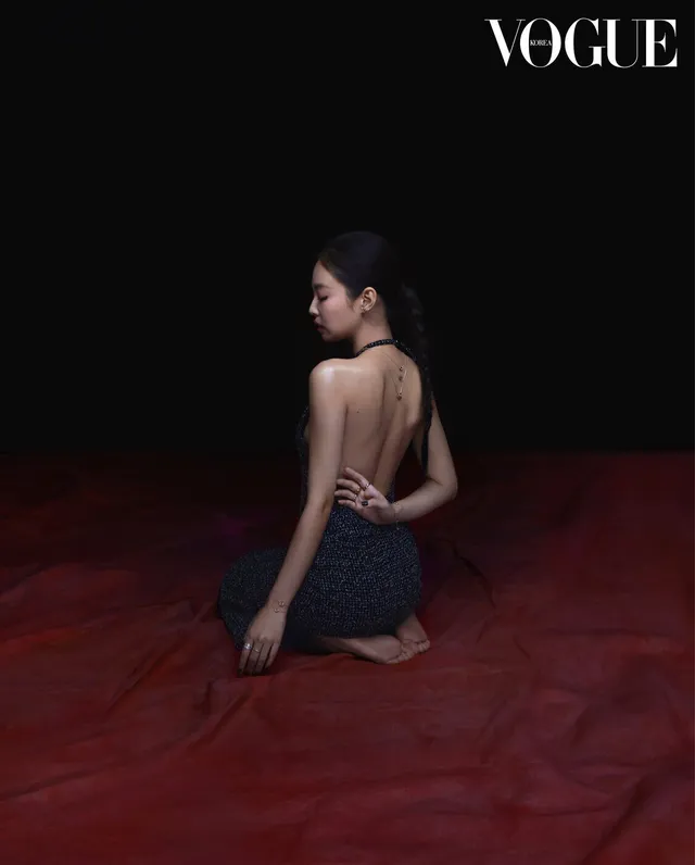 Jennie Kim kneeling barefoot on a studio floor in a dark outfit during a magazine shoot.