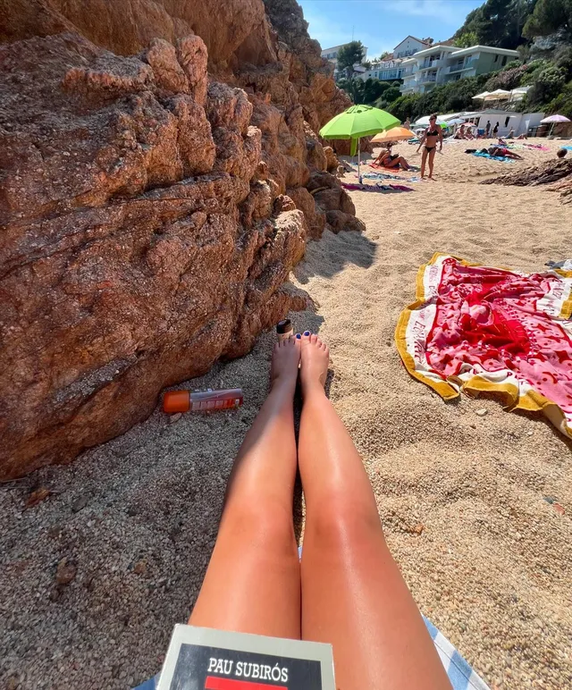 Nicole Wallace shown reclining barefoot on a beach beside a book.