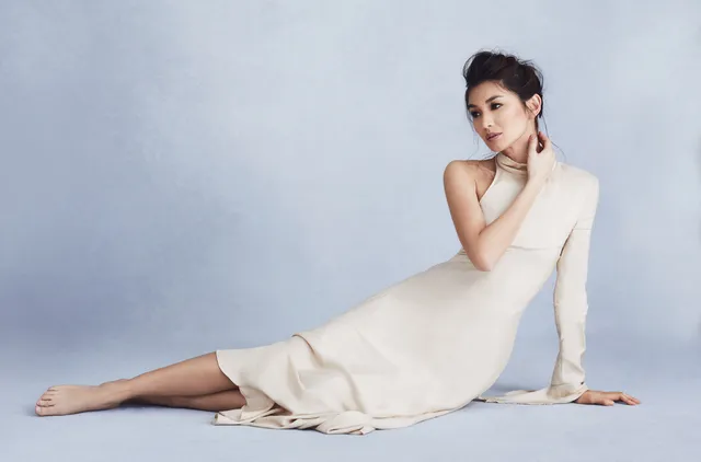 Gemma Chan reclining on the floor in a pale flowing dress.