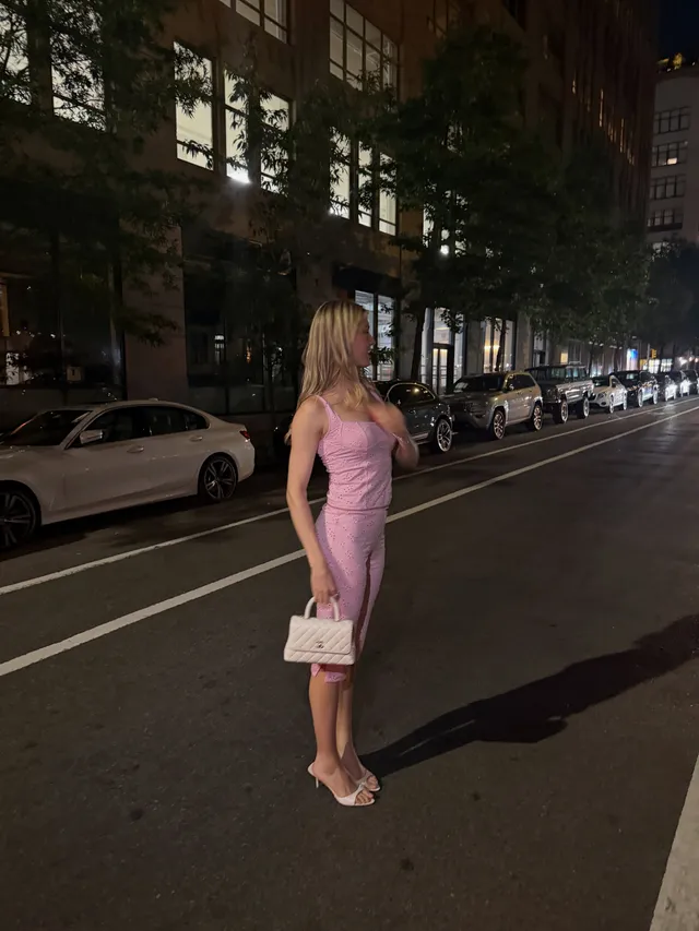 Eugenie Bouchard standing in pale heels and a fitted pink dress outdoors at night.