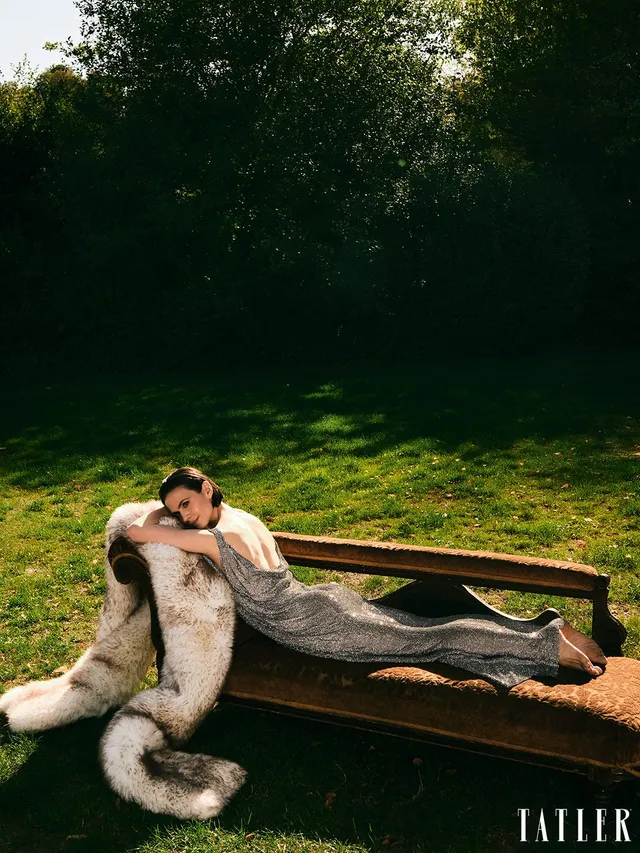 Hayley Atwell reclining on a park bench in a fashion portrait.