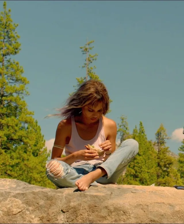 Zoë Kravitz sitting on a rock outdoors in jeans.