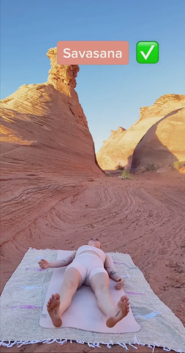 Cara Delevingne lying on a blanket beneath desert rock formations.