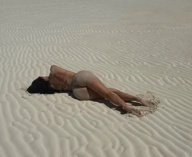 Kylie Jenner lying barefoot on rippled beach sand.