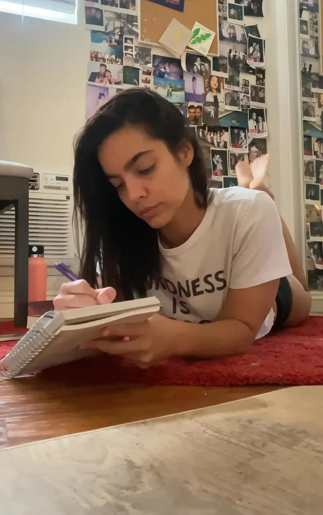 María Gabriela de Faría writing in a notebook while lying barefoot on the floor.