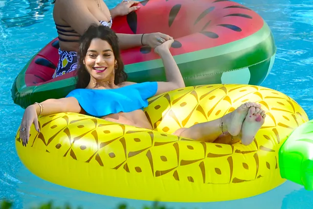 Vanessa Hudgens reclining barefoot on a pineapple pool float.