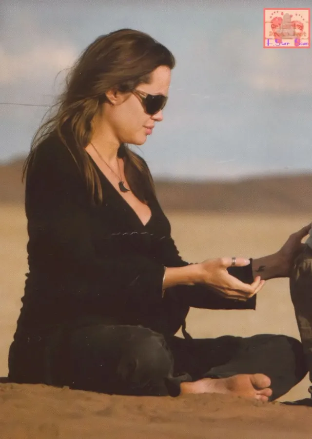 Angelina Jolie seated in dark clothing with her bare feet resting in front of her.