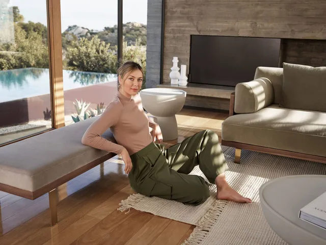 Maria Sharapova sitting barefoot on a wooden seat beside a living-room rug.