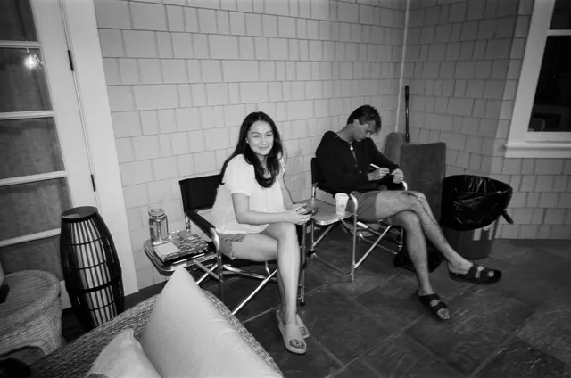 Lola Tung sitting backstage in a white outfit and light-colored heels.