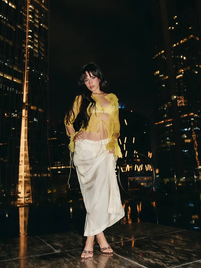 Camila Cabello posing outdoors at night in a white skirt and heels.