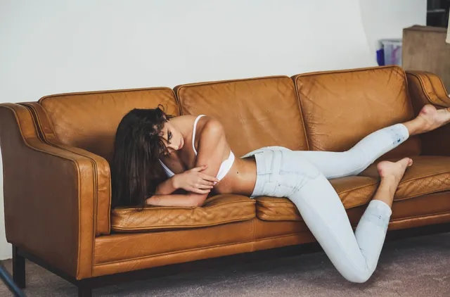 Taylor Hill lying on a leather sofa in jeans with her bare feet raised.