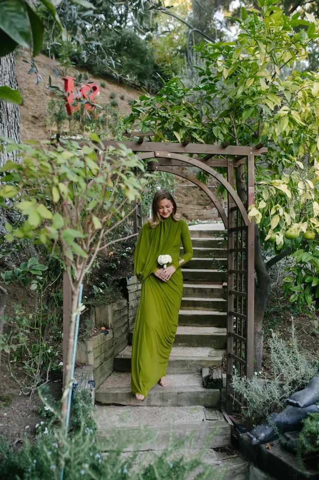 Gigi Hadid standing on garden steps in a long green dress.