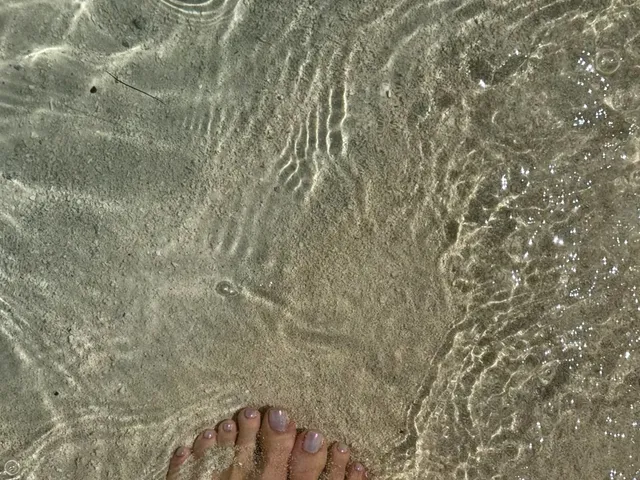 Kylie Jenner standing barefoot in clear shallow water.