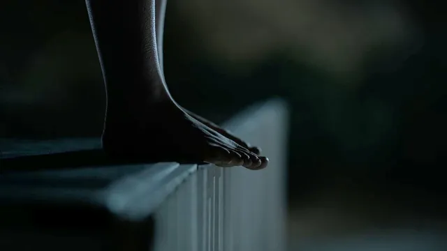 Kiernan Shipka resting a bare foot at the edge of a seat in a film scene.