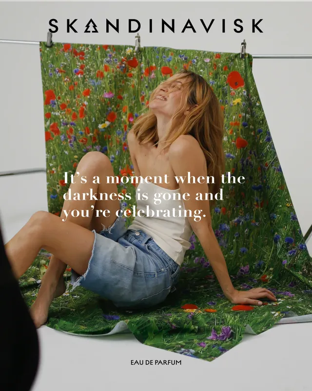 Josephine Skriver reclining barefoot in front of a floral fragrance backdrop.