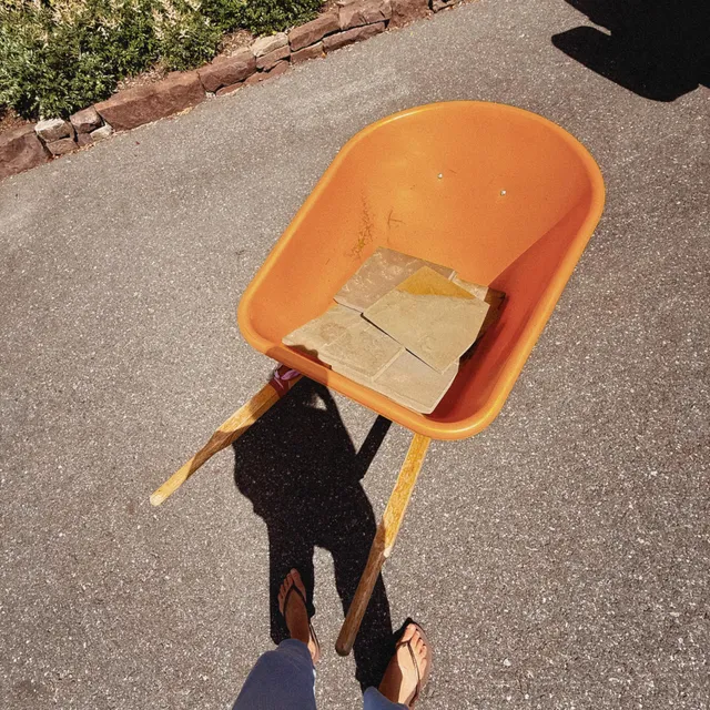 Gigi Hadid wearing flat sandals beside an orange chair.