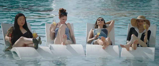 Nina Dobrev sitting barefoot with friends beside the water.