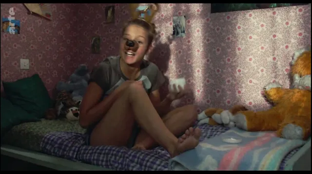 Adèle Exarchopoulos sitting cross legged on a bed in a screen scene.