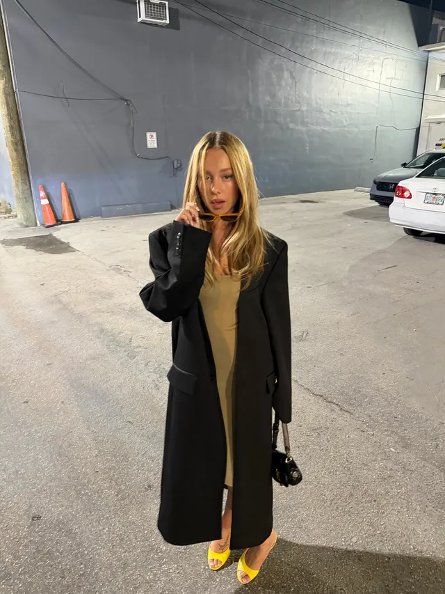 Ester Expósito wearing yellow pointed heels and a dark coat outdoors at night.