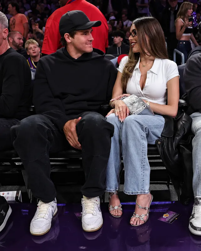 Madison Beer: seated courtside in jeans and pale high heels.