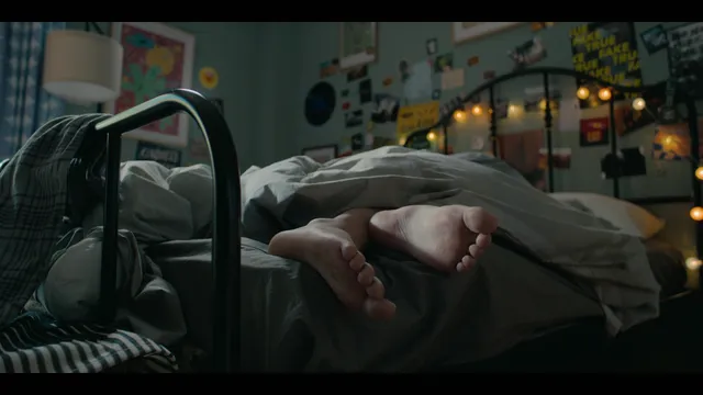 Nicole Wallace reclining on a bed with bare feet visible in a scene.
