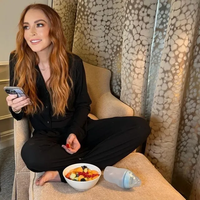 Lindsay Lohan sitting barefoot in black clothing with a bowl of fruit.