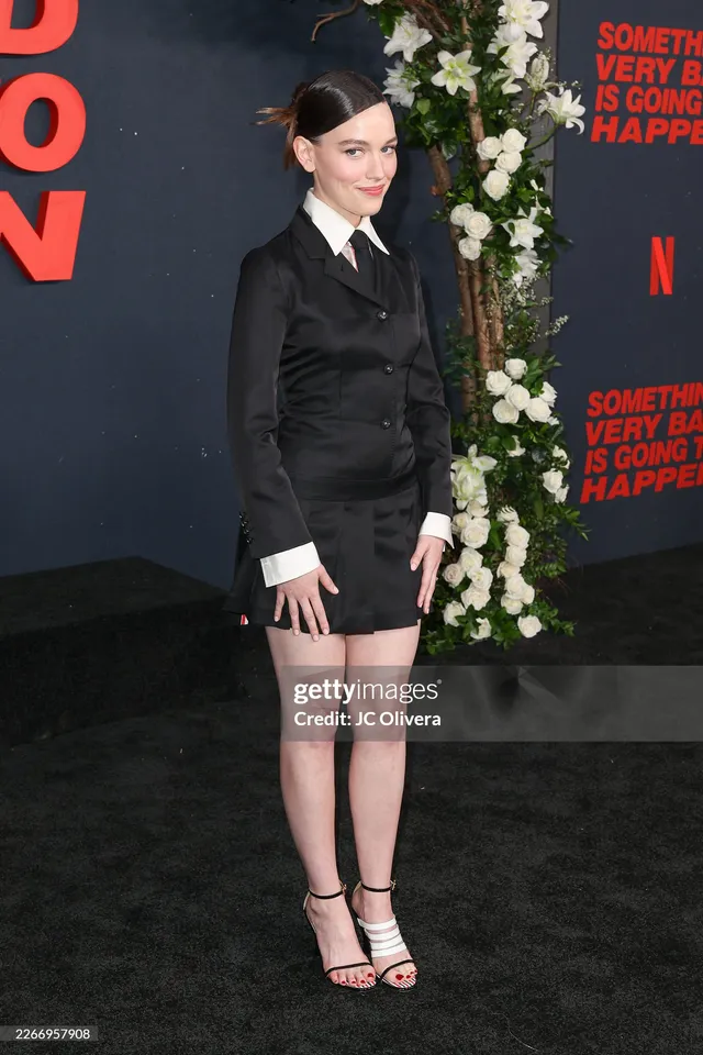 Victoria Pedretti posing at a premiere in a dark tailored outfit.