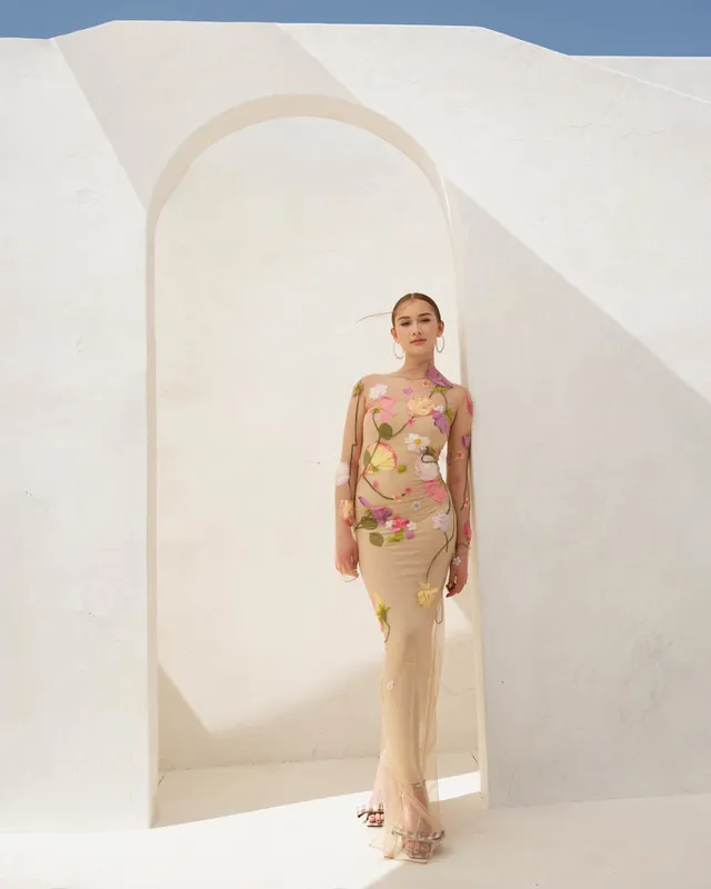 Lola Tung posing in a pale floral dress and platform heels.