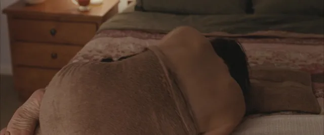 Elizabeth Olsen lying on a bed beneath a brown blanket.