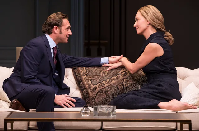 Uma Thurman sitting barefoot on a sofa beside a companion.