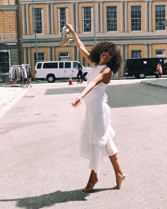 Samantha Logan posing barefoot on a city sidewalk in a pale dress.