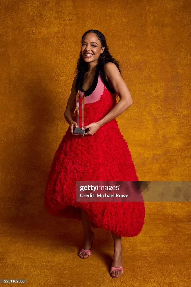 Tessa Thompson smiling in a red dress against a gold background.