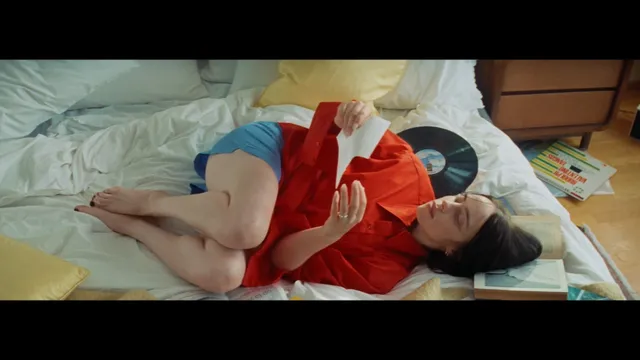 Billie Eilish a reclining screen scene in a red shirt.